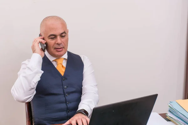 A business man on the phone and pc, at desk, in conference call