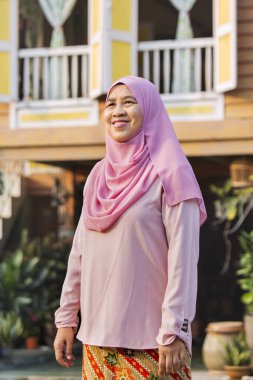 Yaşlı kadın ahşap evin önünde duruyor.