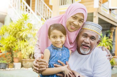 Büyükannesi ve büyükbabasıyla birlikte ahşap evin önünde duran kız.