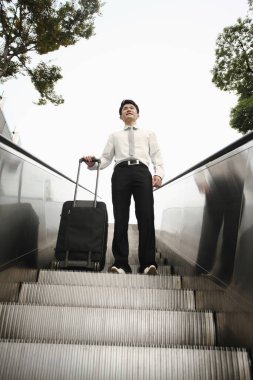 Yürüyen merdivende bavulunu tutan bir iş adamı.
