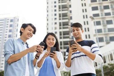 Akıllı telefonlarını kullanan üç genç yetişkin.