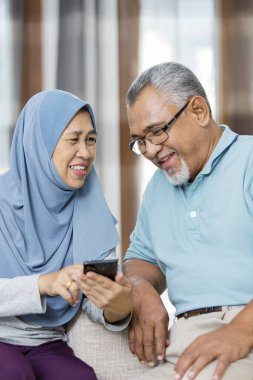 Yaşlı kadın telefonda kocasına bir şey gösteriyor.