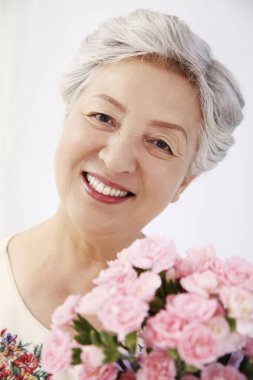 Yaşlı kadın elinde bir buket çiçek tutuyor.