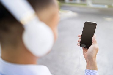 Telefonunu kullanarak kulaklıkla müzik dinleyen bir adam.