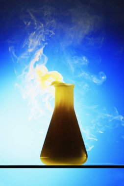 Cam bir şişenin içindeki sarı sıvı dumandan dışarı çıkıyor.