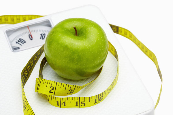 Measuring tape wound around a green apple on a weighing scale