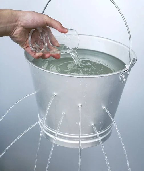 Hand Gießt Wasser Aus Einem Glas Einen Undichten Eimer — Stockfoto