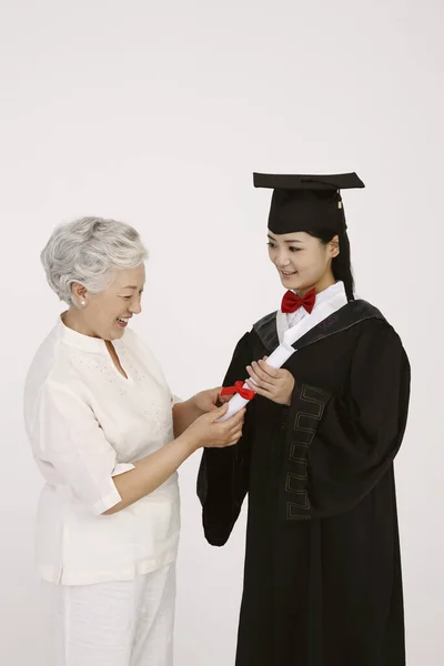 Kobieta Szlafroku Dyplomowym Pokazująca Zwój Starszej Kobiecie — Zdjęcie stockowe