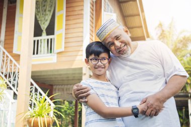 Oğlan büyükbabasıyla ahşap evin önünde.