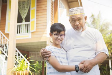 Oğlan büyükbabasıyla ahşap evin önünde.