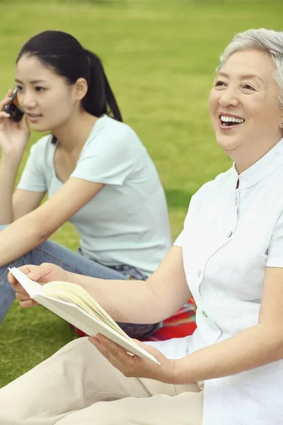 Старша Жінка Тримає Книгу Сміється Поки Жінка Розмовляє Телефону — стокове фото