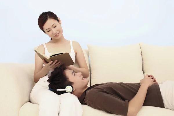 女性の膝の上に横たわっている間 男はヘッドフォンで音楽を聞いて 女性は本を読んで — ストック写真