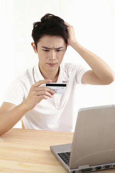 Man frowning and scratching his head while looking at credit card