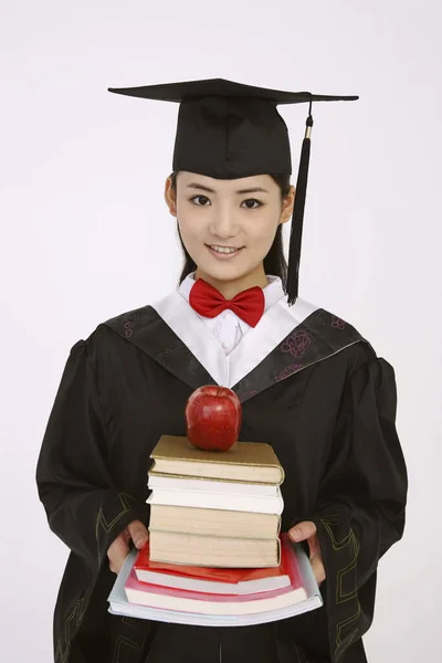 Γυναίκα Ρόμπα Αποφοίτησης Κρατώντας Στοίβα Από Βιβλία Μήλο Στην Κορυφή — Φωτογραφία Αρχείου