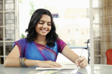 Tebrik kartı yazarken gülümseyen genç kız.