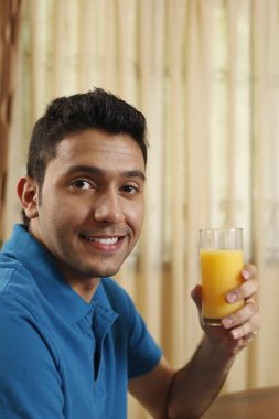 Adam elinde bir bardak portakal suyu tutarken gülümsüyor.