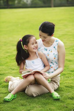 Anne ve kızı parkta kitap okuyorlar.