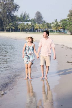 Erkek ve kadın sahilde yürürken el ele tutuşuyorlar.