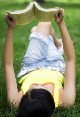 Sahada uzanmış kitap okuyan genç bir kadın.