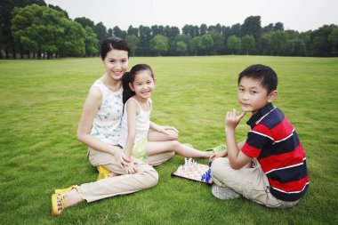 Anne ve çocuklar parkta satranç oynuyorlar.