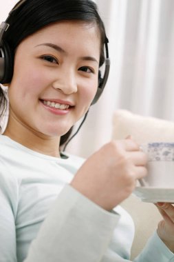 Kadın kulaklıkla müzik dinlerken bir fincan kahveden zevk alıyor.