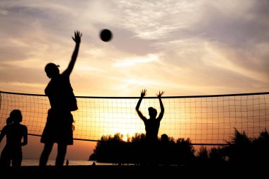 Plaj voleybolu oynayan kadın ve erkeklerin silueti.
