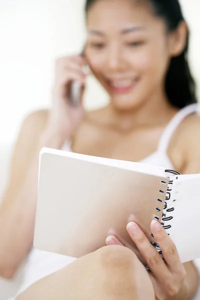 Kobieta Patrząc Notatnik Podczas Rozmowy Przez Telefon — Zdjęcie stockowe