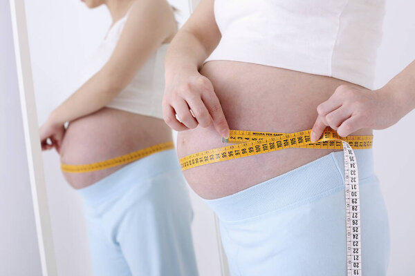 беременная женщина измеряет ее желудок