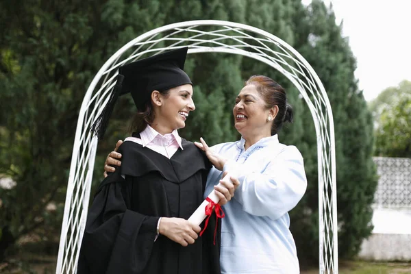 Senior woman and woman in graduation gown smiling at each other