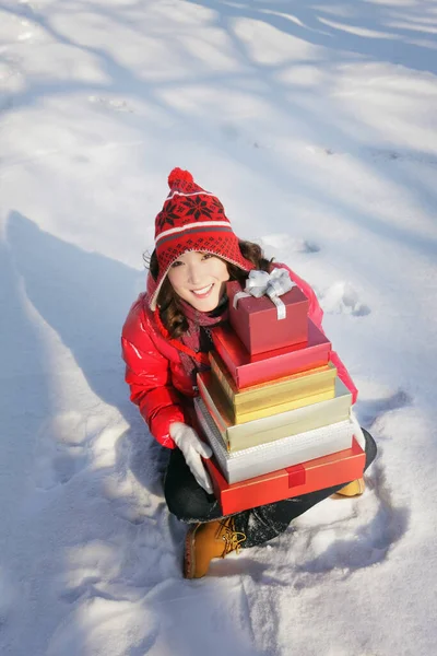 穿着保暖衣服的女人坐在雪地上 手里拿着一堆礼品盒 — 图库照片