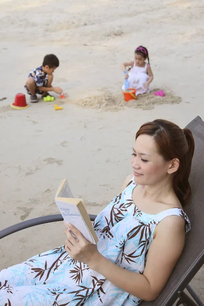 Женщина Сидит Пляже Кресло Читает Книгу Мальчик Девочка Играют Песком — стоковое фото