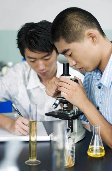 Young Man Looking Microscope His Course Mate Making Notes — Stock Photo, Image