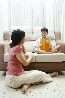 Anne oğlunun kitap okumasına bakıyor.