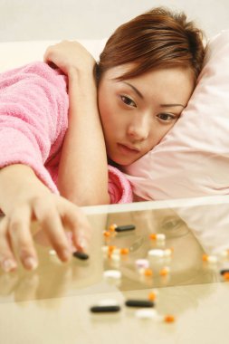 Kanepede uzanmış kahve masasındaki dağınık haplara ulaşmaya çalışan bir kadın.