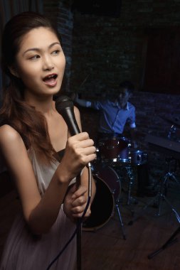 Kadın şarkı söylüyor, erkek arkada davul çalıyor.