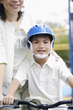 Anne oğlunun bisiklete binmesine yardım ediyor.