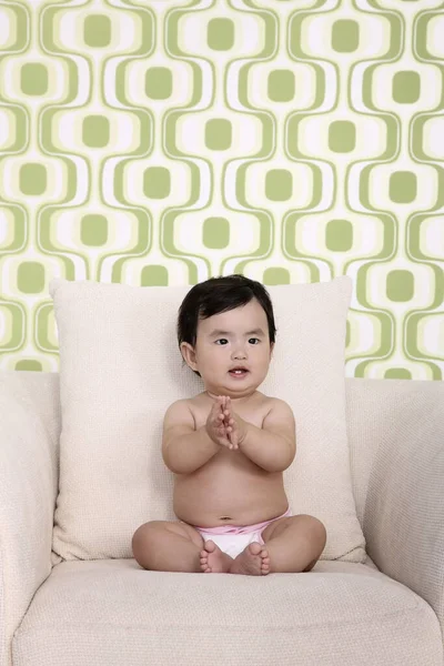 赤ちゃん女の子座っています上のソファとともに手クラップ — ストック写真