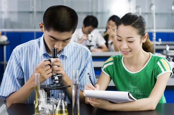 Young Woman Making Notes While Young Man Looking Microscope — Stock Photo, Image