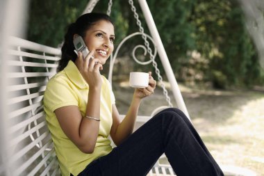 Kadın telefonda konuşurken bir fincan kahveden hoşlanıyor.