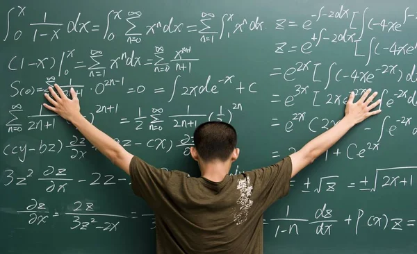 数式でいっぱいの黒板に固執する若い男 — ストック写真