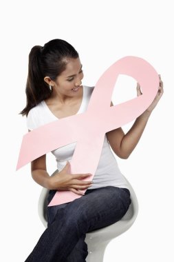 Sandalyede oturan mutlu kadın pembe göğüs kanseri kurdelesini tutuyor.