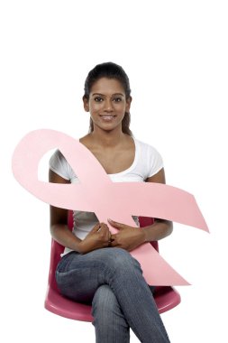 Sandalyede oturan mutlu kadın pembe göğüs kanseri kurdelesini tutuyor.