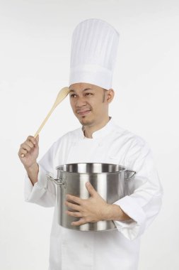 Asyalı aşçı elinde güveç tenceresi ve tahta kaşıkla stresli görünüyor.