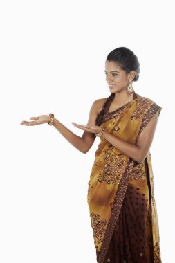 Sari giymiş bir kadın el hareketleriyle gülümsüyor.