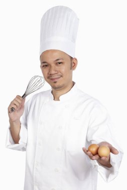 Her iki elinde çırpı ve yumurta olan Asyalı şef.