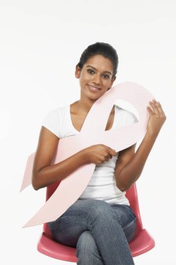 Sandalyede oturan mutlu kadın pembe göğüs kanseri kurdelesini tutuyor.