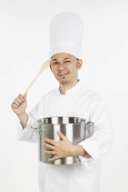 Asyalı aşçı elinde güveç tenceresi ve tahta kaşıkla stresli görünüyor.