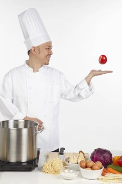 Asyalı şef sağlıklı bir yemek hazırlıyor, havada domates atıyor.