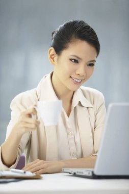 İş kadını içki içerken dizüstü bilgisayarda çalışıyor