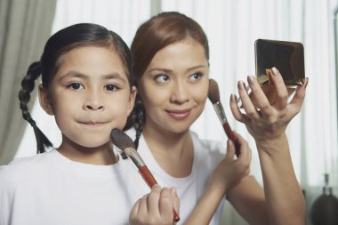 Anne ve kızı yüzüne makyaj yapıyor.